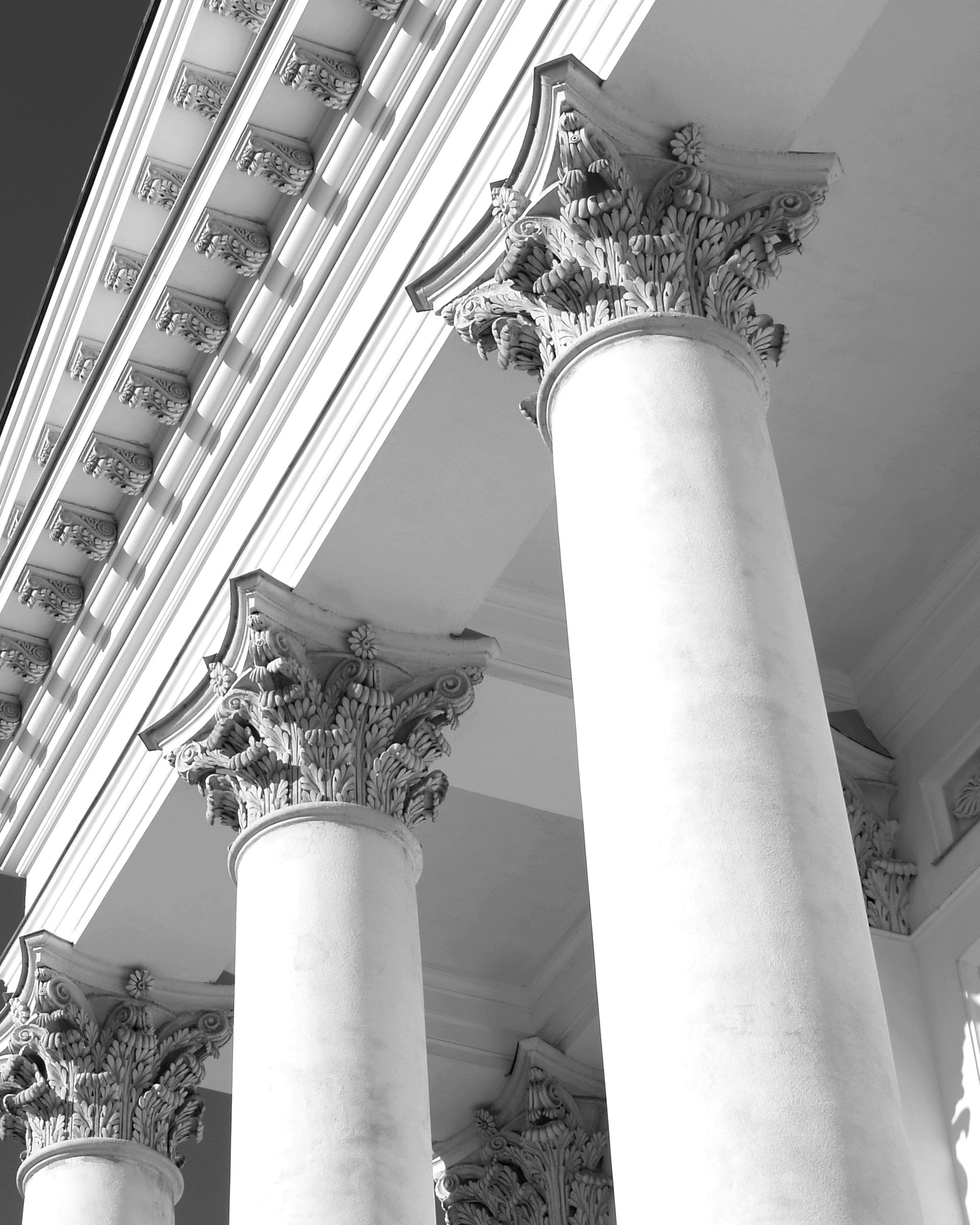 Corinthian capitals and a carved cornice seen from below, in black and white.